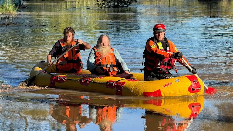 Two NSW SES volunteers rescuing a man while rowing a boat.