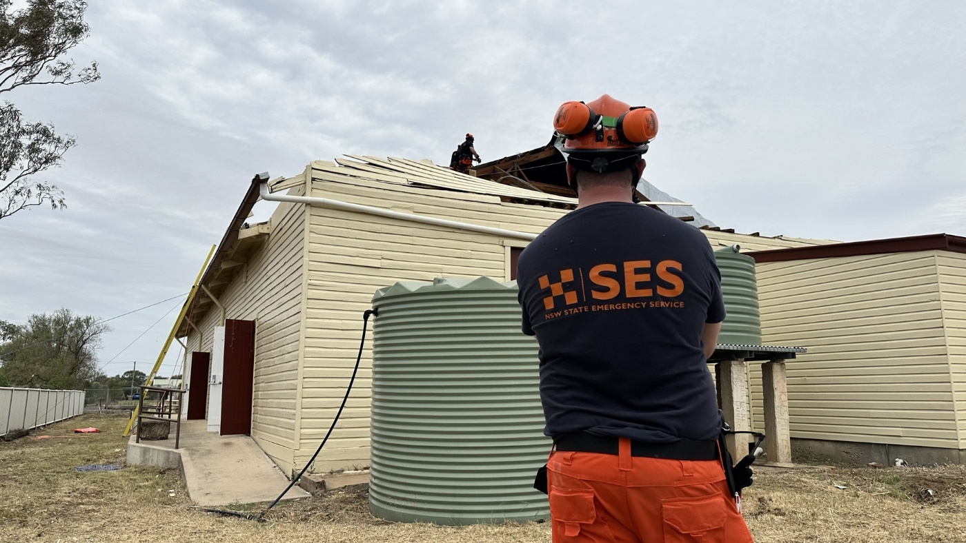 NSW SES volunteer standing on the groud and look at a damaged roof after a storm